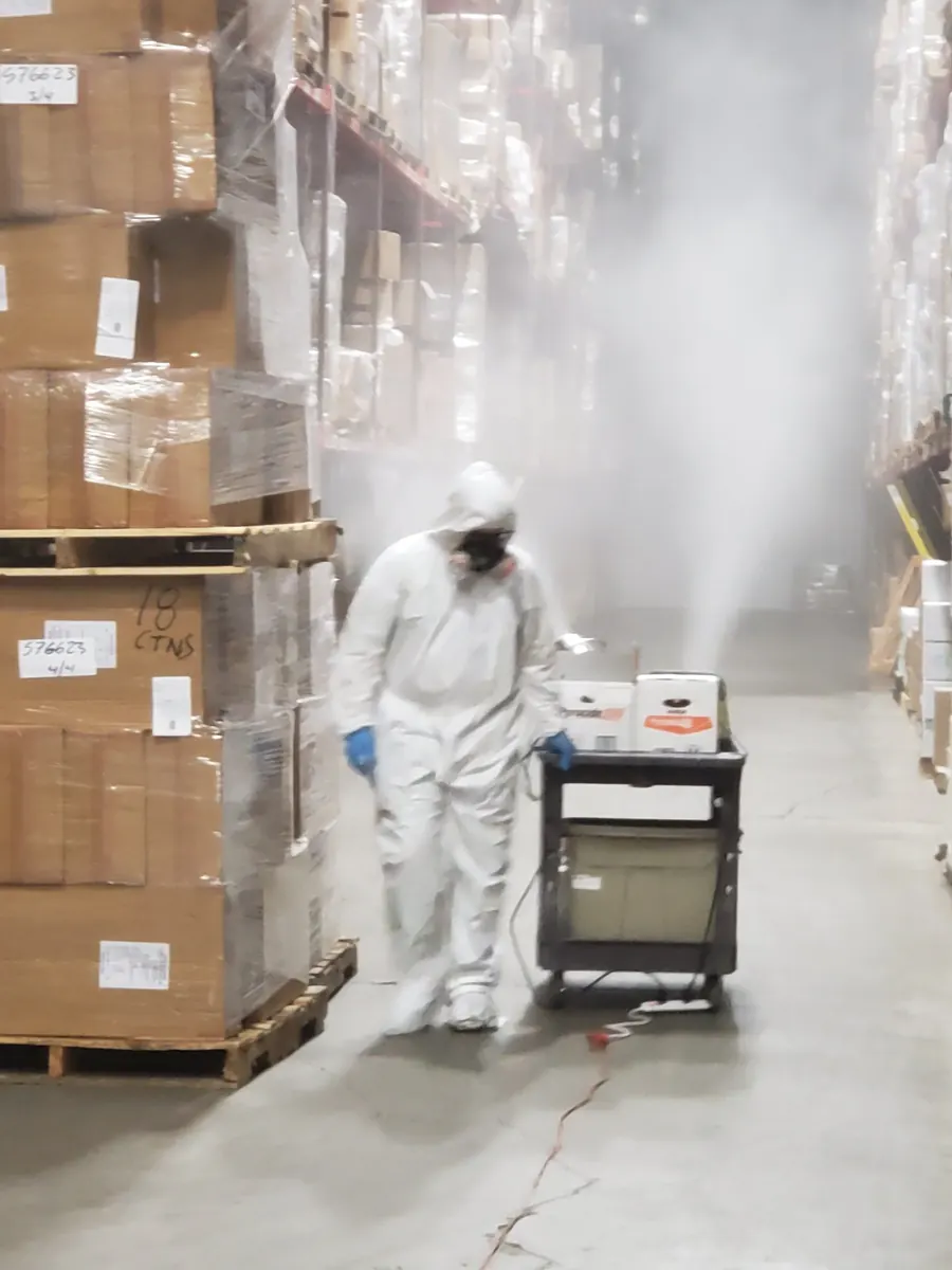 A Marrone technician in protective equipment fogging a warehouse aisle